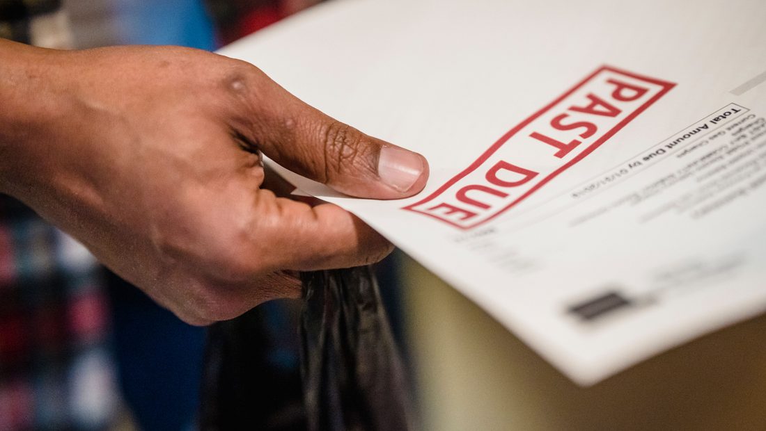 A hand holding a bill stamped PAST DUE in red