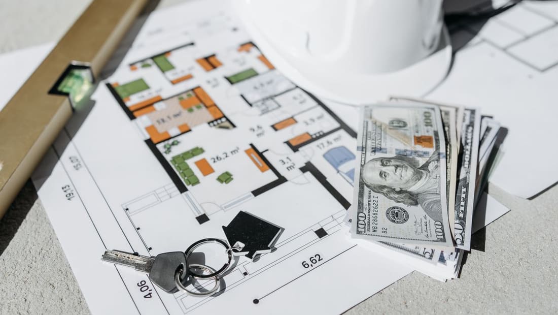 A stack of cash and house keys on a home floor plan