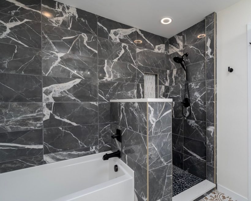 Renovated bathroom with black marble tile and a glass shower by House Buyers of Cheyenne